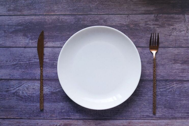 Ein weißer, leerer Teller mit Besteck auf einem grauen Untergrund.