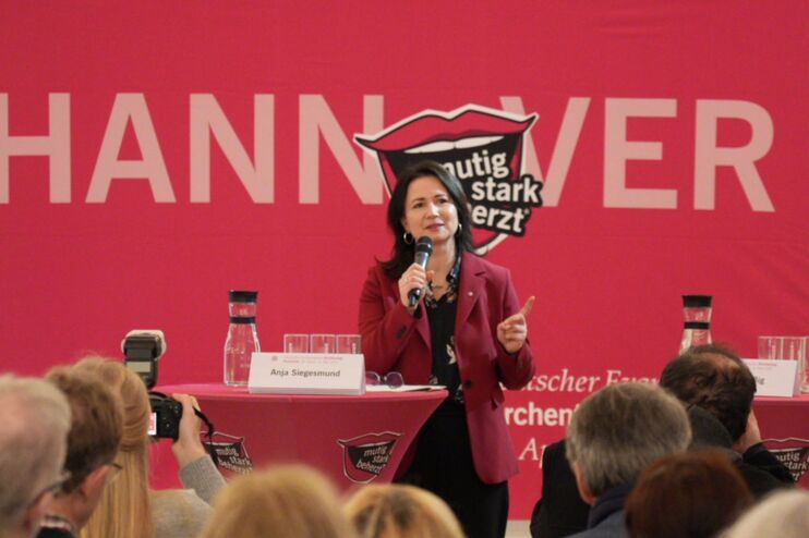 Eine Frau steht vor einem rotem Banner mit dem Kirchentags-Logo, darüber steht Hannover.