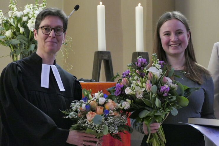 Zwei Frauen, eine mit Talar und eine andere mit Blumenstrauß.
