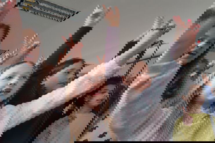 Aus der Froschperspektive: Kinder recken die Arme in die Höhe und schauen fröhlich.