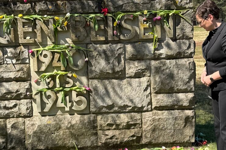 Eine Frau steht vor einem Gedenkstein, darauf steht Bergen Belsen 1940 bis 1945.