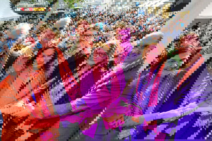 Mehrere Menschen halten einen Staffelstab in die Höhe. Manche tragen rote Schals.