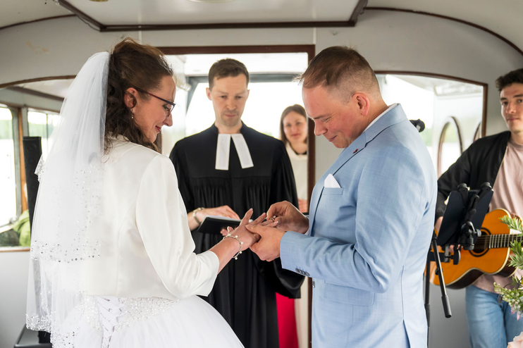 Ein Brautpaar steht in einem Schiff und wird von einer Person im Talar gesegnet. 