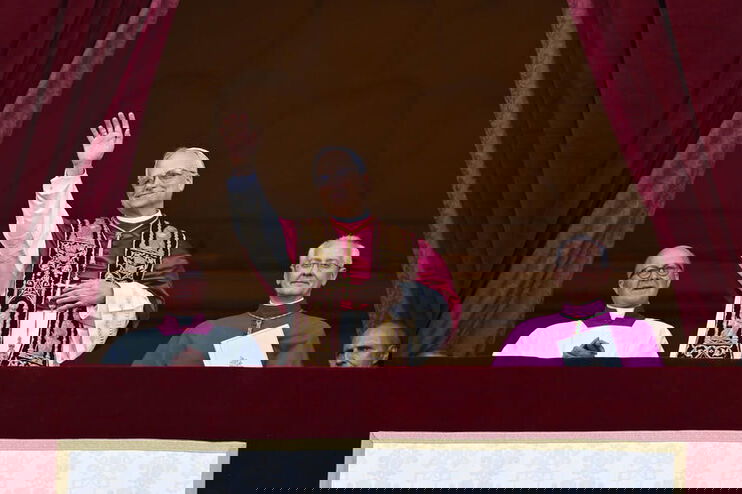 Eine ältere männlich zu lesende Person steht auf einem Balkon und winkt.