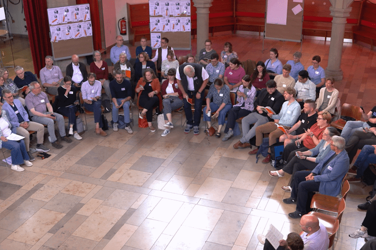 Viele Menschen sitzen im Halbkreis in einer Kirche.