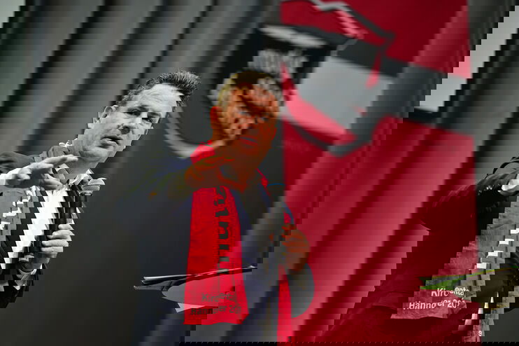 Eine als Mann lesbare Person mit einem Kirchentagsschal spricht in ein Mikrofon und gestikuliert.