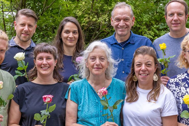 Ein Gruppenfoto, die Personen lächeln und halten Blumen