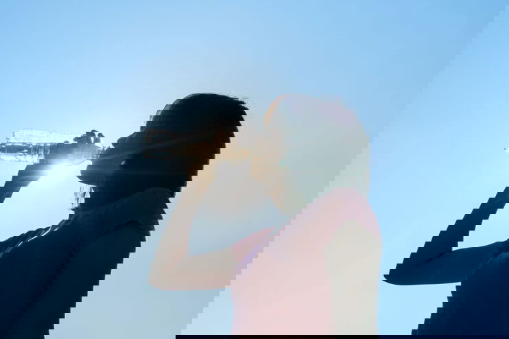 Eine als Frau lesbare Person trinkt aus einer Wasserflasche.