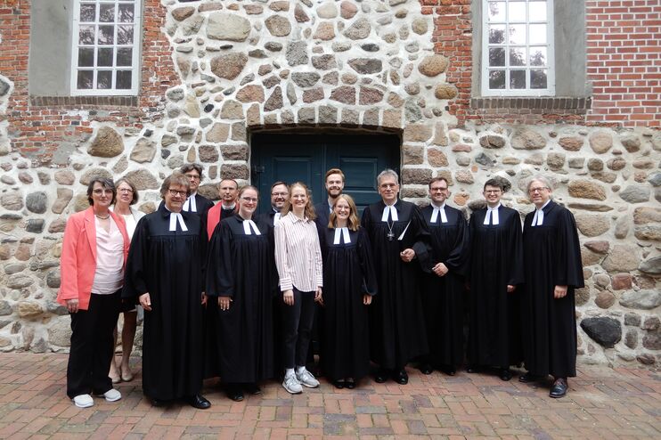 Mehrere Menschen, die meisten im Talar, vor einer Kirche aus großen Steinen. 