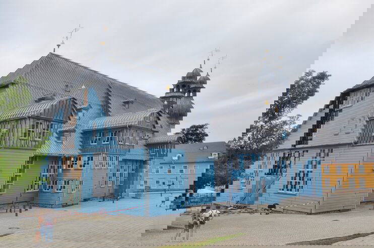 Ein hellblaues Holzgebäude (eine Kirche), deren Fassade an der kurzen Seite beschädigt ist. 