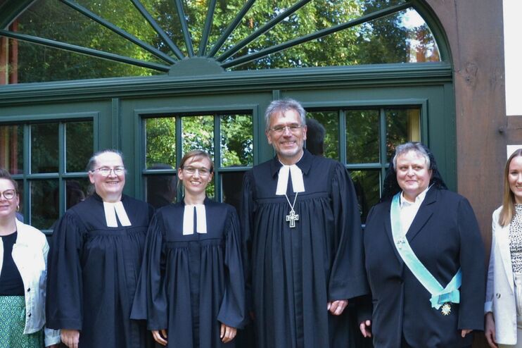 Menschen in festlicher Kleidung oder Talar vor einer Kirche.