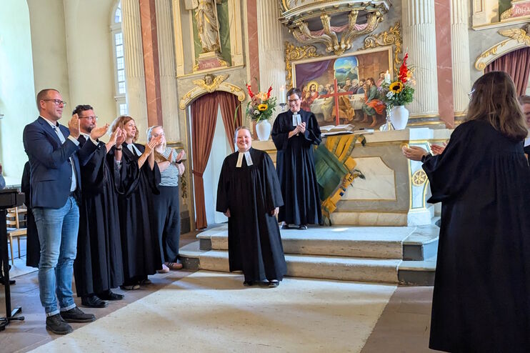 Mehrere Menschen applaudieren einer weiblich gelesenen Person im Talar in einer Kirche.