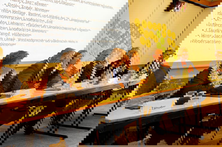 An einem langen Tisch sitzen mehrere Menschen und diskutieren.