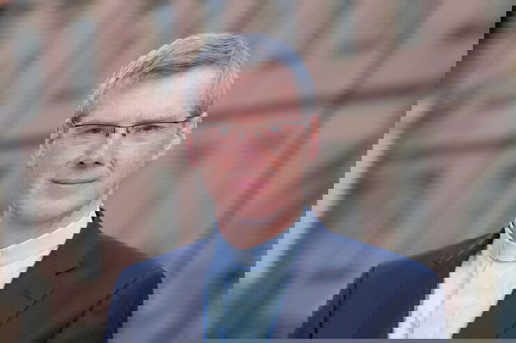 Eine mittelalte als Mann lesbare Person im hellblauen Collarhemd.