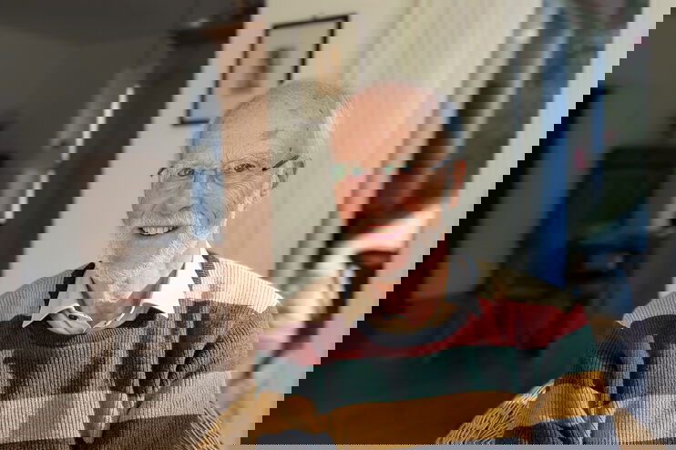 Eine als Mann lesbare ältere Person im Wohnzimmer.