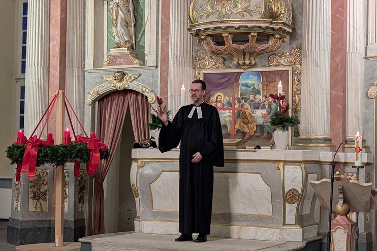 Eine männlich gelesene Person im Talar steht vor dem Altar in einer Kirche.