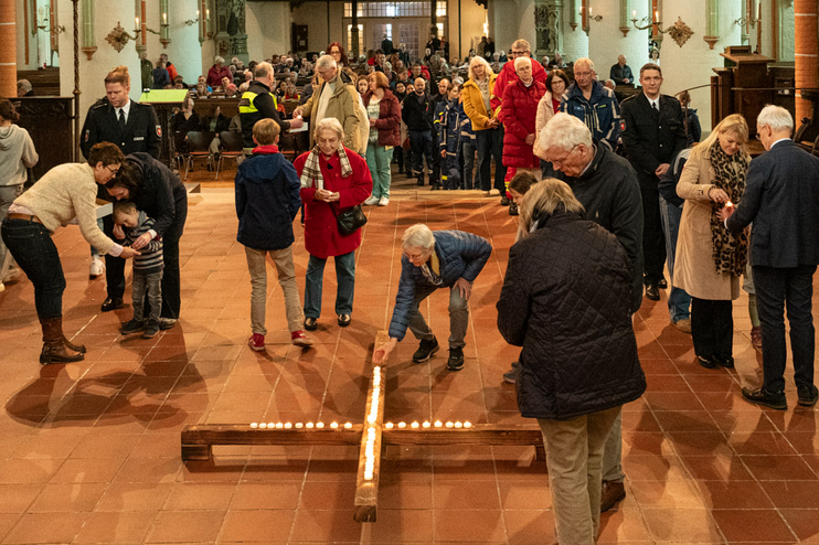 Blick in eine Kirche, in der Menschen mit Kerzen ein Kreuz legen.