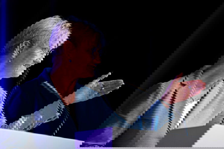 Eine weiblich gelesene Person mit blauem Blazer an einem Mikro.