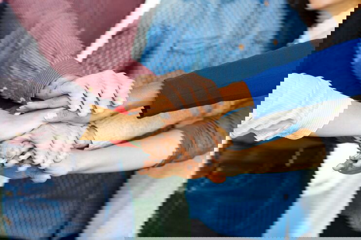 Mehrere Menschen unterschiedlicher Hautfarben legen ihre Hände übereinander.