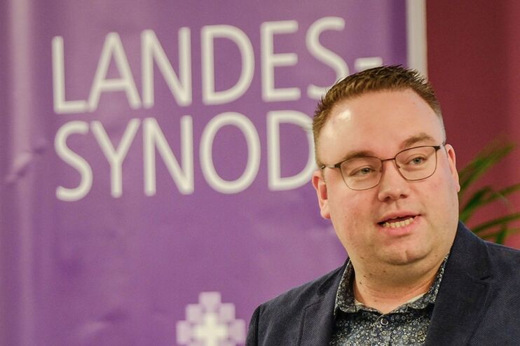 Ruben Grüssing vor dem lila Banner der Landessynode.