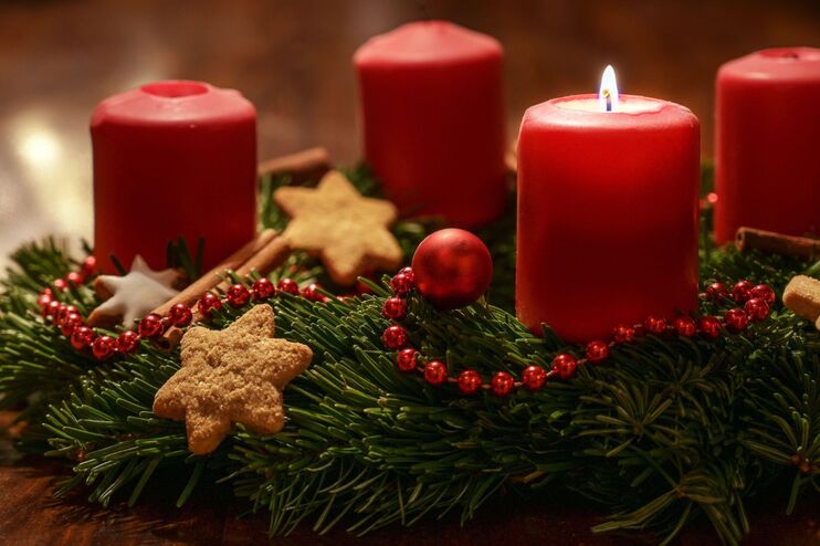 Ein Adventskranz mit roten Kerzen, bei dem eine Kerze brennt.