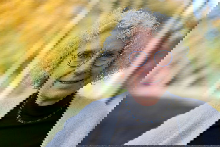 Eine als Frau lesbare Person mit grauen Locken und Brille.