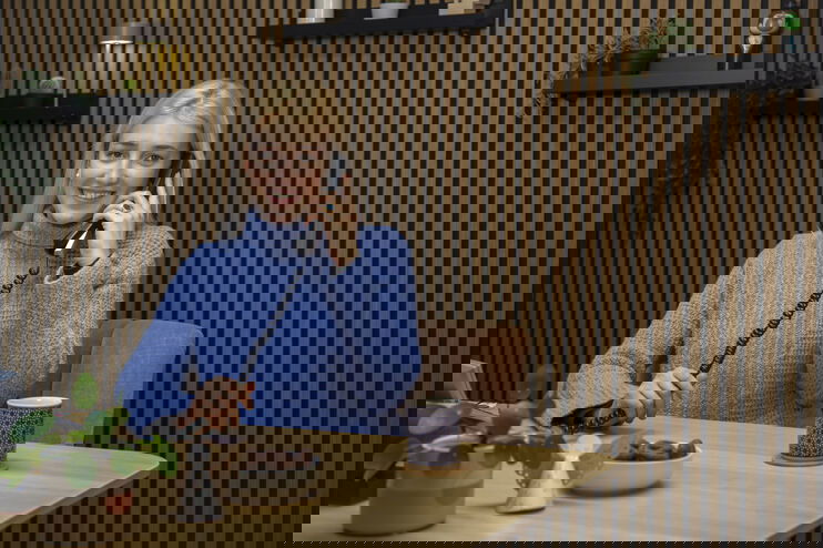 Eine als Frau lesbare Person sitzt an einem Tisch und telefoniert.