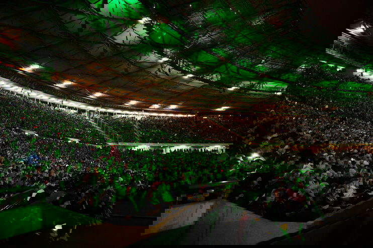Viele tausend Menschen in einem grün erleuchteten Stadion.