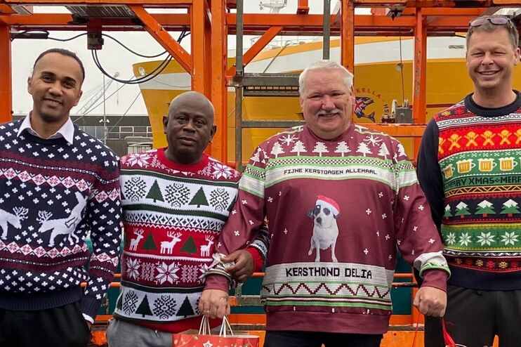 Vier Männer tragen Weihnachtspullover und Geschenktüten.