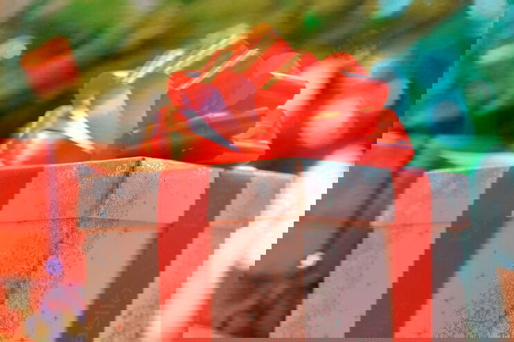 Ein weiß-silberner Karton mit roter Schleife vor einem Weihnachtsbaum.