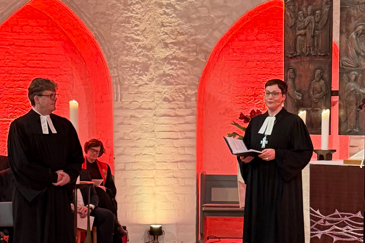 Zwei Personen in Talaren in einer rot erleuchteten Kirche.