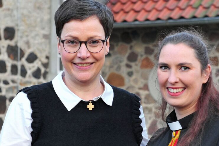 Zwei als Frauen lesbare Personen vor einer Kirche.