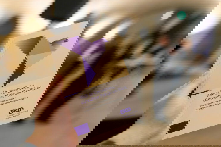 Eine Hand hält ein Buch mit der Aufschrift „Welt in Unordnung – Gerechter Friede im Blick“