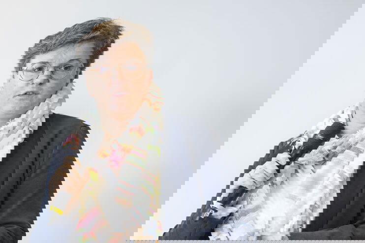 Eine weiblich gelesene Person mit blauer Jacke und Schal hält ein Mikro in der Hand.