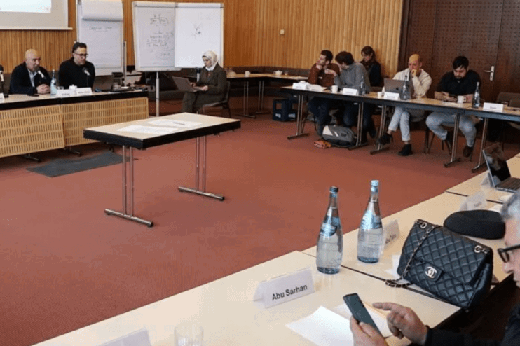 Blick in einen Konferenzraum, in dem etwa ein Dutzend Personen sitzen.