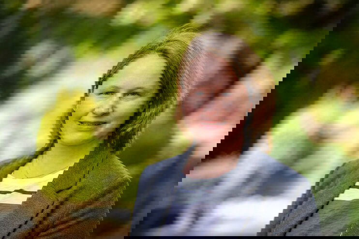 Portraitfoto einer als Frau lesbaren Person vor einem grünen Hintergrund