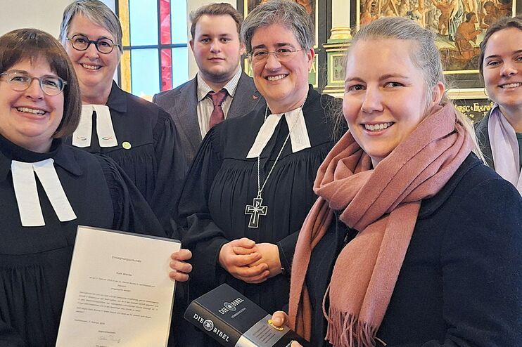 Menschen stehen mit einer Urkunde und Bibel und zum Teil im Talar in einer Kirche.