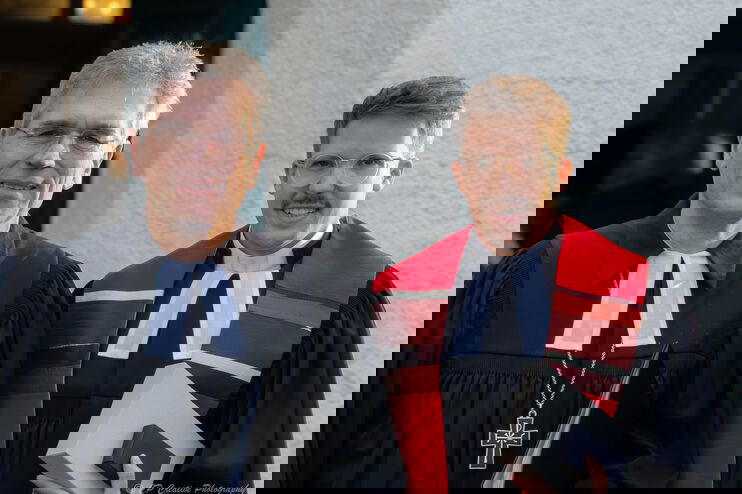 Zwei männlich gelesene Personen mit Talaren vor einer Kirche.