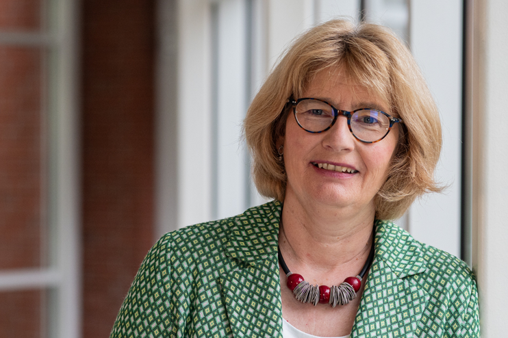 Eine weiblich gelesene Person mit blonden Haaren, grünem Jackett und Brille.