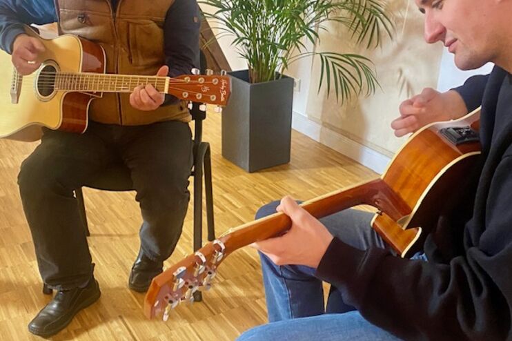 Zwei Personen sitzen sich gegenüber und spielen jeweils Gitarre.