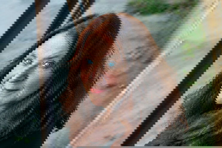 Eine als Frau lesbare Person mit schulterlangen rotbraunen Haaren.