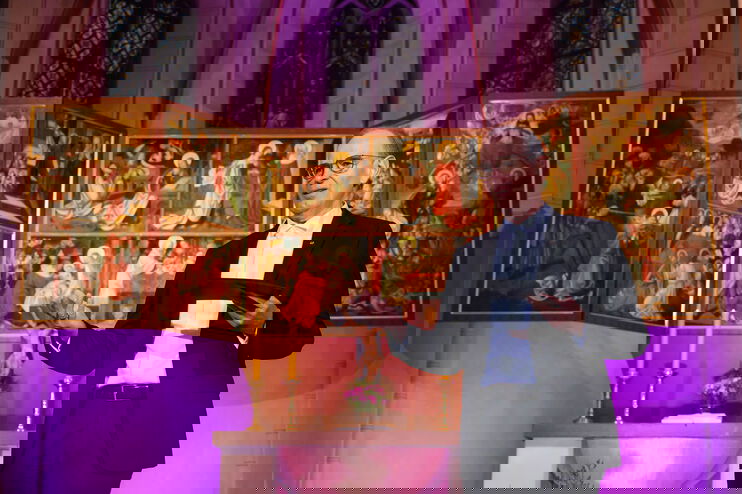 Eine als Mann lesbare Person spricht vor einem Altar.