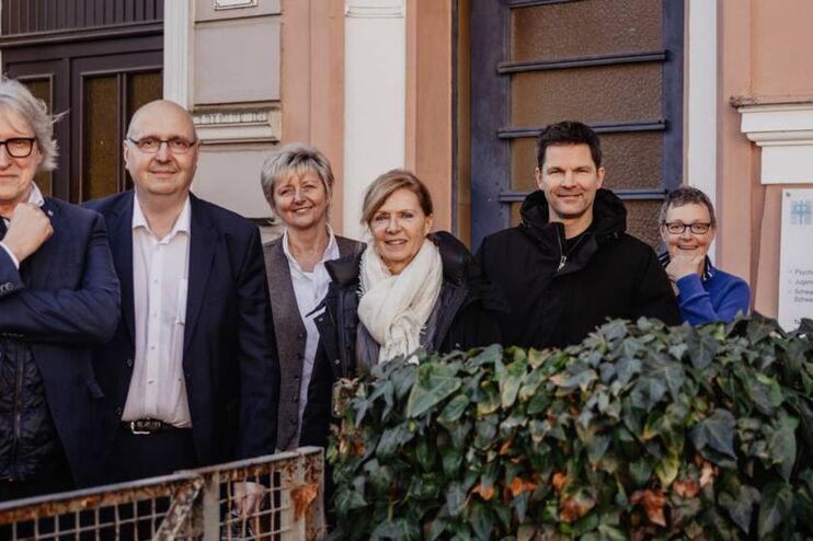 Eine Gruppe aus als Männer und Frauen lesbare Personen steht vor einem Haus der Diakonie.