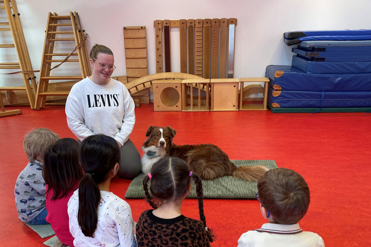 Ein Hund liegt auf einer Matte neben Kindern und einer erwachsenen Person.