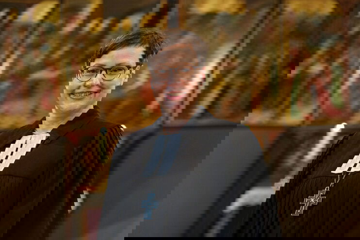 Eine als Frau lesbare Person im Talar und mit Bischofskreuz steht in einer Kirche.