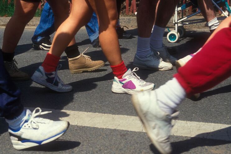 Nahaufnahme mehrerer Beinpaare, die eine Straße entlanglaufen.