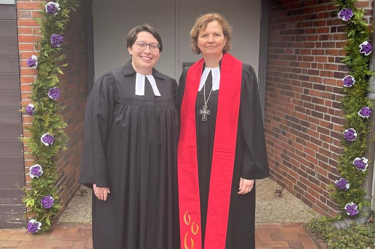 Zwei Frauen im Talar vor einem Blumenbogen