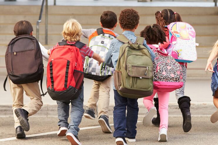 Kinder mit Schulranzen rennen auf dem Schulhof umher.