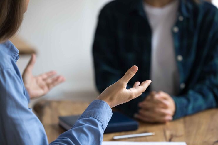 Zwei Personen sitzen an einem Tisch und reden. Eine gestikuliert. Die Köpfe sind nicht zu sehen.
