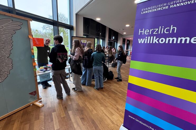 Mehrere junge Menschen stehen an einem Infostand, umrahmt von Rollups.